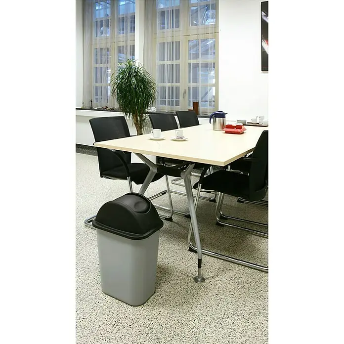 Proregal Standard-Mülleimer Rubbermaid rechteckiger Abfallbehälter - 39 l, Kunststoff, Grau - Ein grauer Schwingdeckeleimer aus Kunststoff steht neben einem Konferenztisch. Praktisch und unauffällig für den Büroalltag.