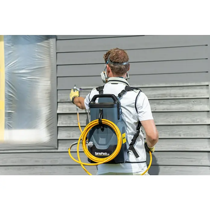 Akku-Farbsprühsystem - 18 V, 1 Akku, 4 Ah, Max. Fördermenge: 0,9 l/min - Ein Mann sprüht Farbe mit einem Wagner Spraypack Farbsprühgerät auf eine Hauswand. Das Gerät ist auf seinem Rücken befestigt.