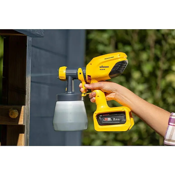 Wagner Akku-Farbsprühsystem Wood&Metal Sprayer W 250 18V - 18 V, Ohne Akku - Eine gelbe Wagner Farbspritzpistole wird von einer Person gehalten. Das Gerät verfügt über einen Behälter und einen Akku.