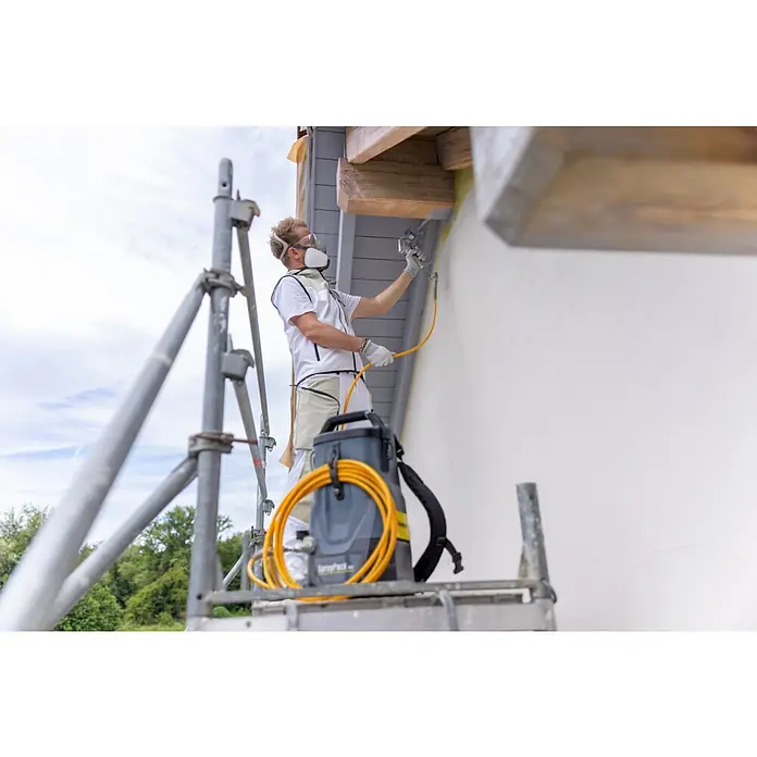 Akku-Farbsprühsystem - 18 V, 1 Akku, 4 Ah, Max. Fördermenge: 0,9 l/min - Ein Handwerker auf einem Gerüst, der eine Außenwand mit einem Farbsprühgerät und einem Spritzgerät im Rucksack lackiert.