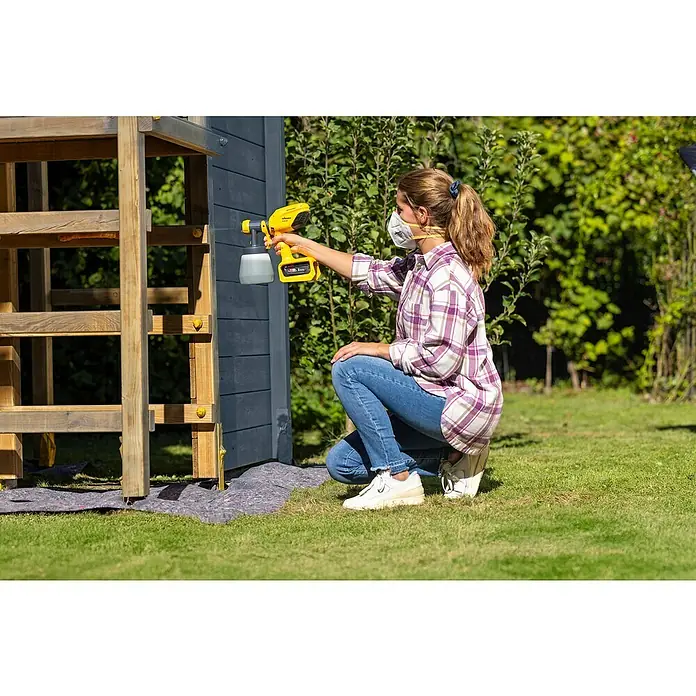 Wagner Akku-Farbsprühsystem Wood&Metal Sprayer W 250 18V - 18 V, Ohne Akku - Frau benutzt eine Wagner Farbspritzpistole, um ein Holzhaus im Garten zu streichen, mit Fokus auf die Spritzpistole.