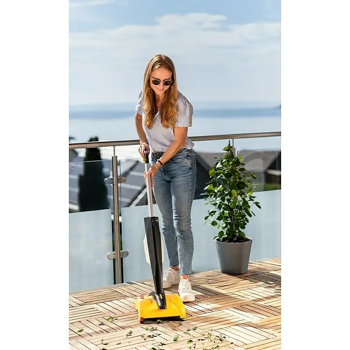 Wagner Akku-Terrassenreiniger Levaro PowerBrush 18V - 18 V, Ohne Akku, 700 l - Frau reinigt mit einer gelb-schwarzen Kehrmaschine eine Holzterrasse mit Blick auf den See.