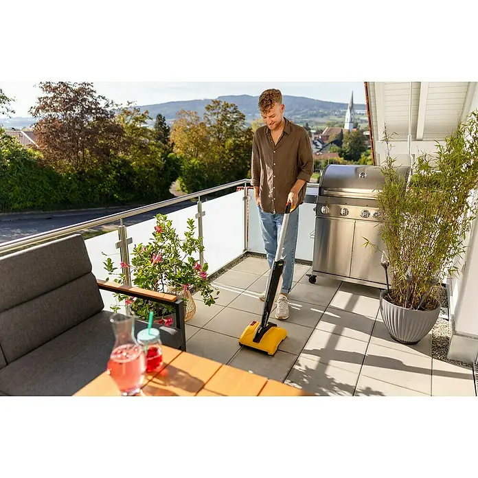 Wagner Akku-Terrassenreiniger Levaro PowerBrush 18V - 18 V, Ohne Akku, 700 l - Ein Mann benutzt einen gelben Akku-Besen auf einer Terrasse mit Grill und Pflanzen. Der Akku-Besen ist das Hauptprodukt im Fokus.