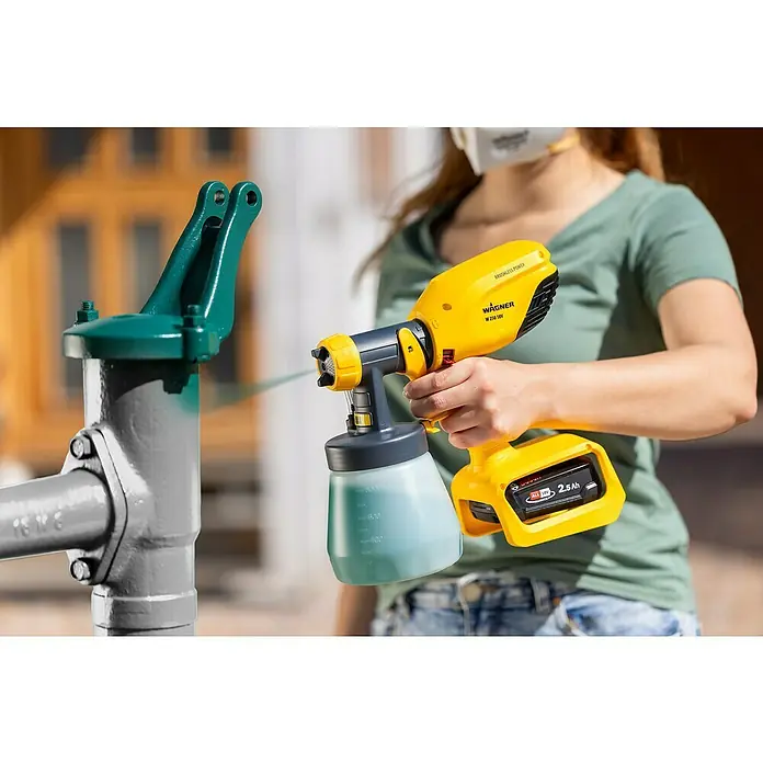 Wagner Akku-Farbsprühsystem Wood&Metal Sprayer W 250 18V - 18 V, Ohne Akku - Eine Frau verwendet eine gelbe Wagner Farbspritzpistole, um ein Metallrohr zu lackieren. Das Gerät ist kabellos und mit einem Akku ausgestattet.