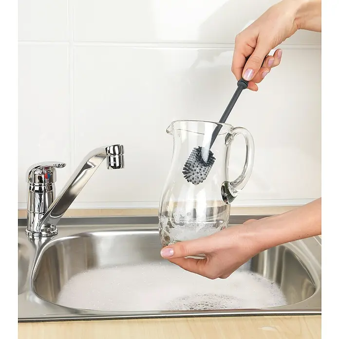Wenko Spülbürste - Länge: 25 cm, Silikon - Glasreinigung leicht gemacht! Eine Person verwendet eine Bürste zum Reinigen einer gläsernen Karaffe in einem Spülbecken voller Seifenwasser.