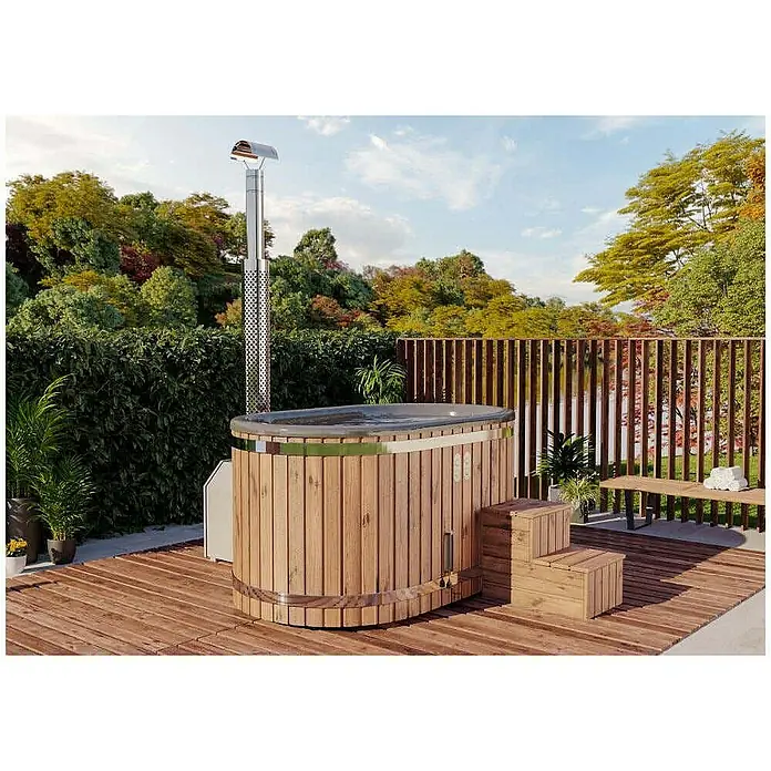 FinnTherm Hot Tub Malmö "Spa Edition" - Nordische Holz, Naturbelassen - Ein ovaler, holzbefeuerter Badezuber mit Edelstahlschornstein auf einer Holzterrasse, umgeben von üppigem Grün.