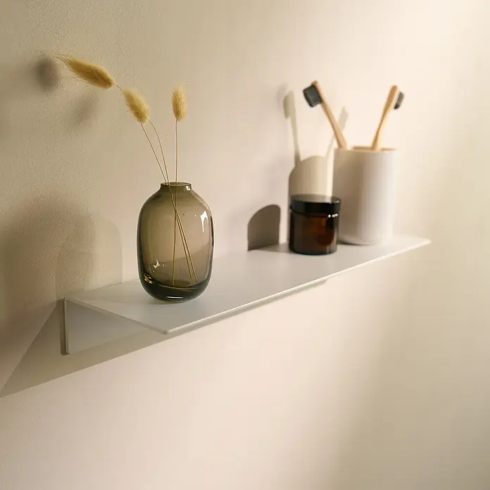 Designfabrik Hamburg Badablage - Breite: 42 cm, Aluminium, Weiß - Ein schlanker, weißer Wandregal mit einer grauen Vase, einer braunen Dose und einem Becher mit Zahnbürsten. Die minimalistische Ästhetik betont das moderne Baddesign.