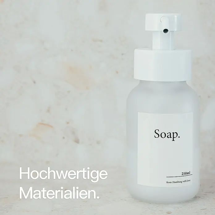 Designfabrik Hamburg Seifenspender - Edelstahl, Weiß/Satiniertes Glas - Eine weiße Seifenflasche mit minimalistischem Design, beschriftet mit "Soap.", steht vor einem hellen Hintergrund.