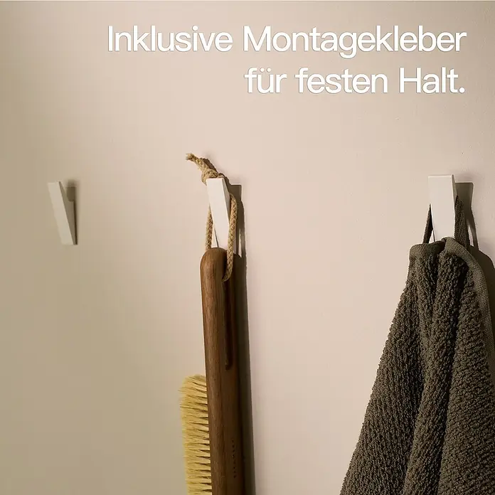 Designfabrik Hamburg Handtuchhaken - 4 Stk., Weiß, Matt - Das Bild zeigt drei weiße Klebehaken an einer Wand, an denen ein Handtuch, eine Bürste und ein leerer Haken hängen.