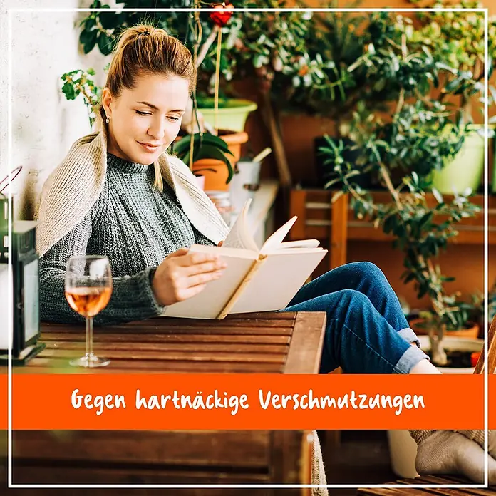 Poliboy Holzreiniger Möbel und Böden - 500 ml, Flasche - Eine Frau liest entspannt ein Buch auf einer Holzterrasse. Im Vordergrund steht ein Glas Roséwein, während im Hintergrund üppige Pflanzen zu sehen sind.