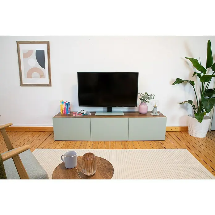 D-c-fix Klebefolie Kreativ-Kit - 3 Stk., 2 m x 67,5 cm, Flagstaff Oak/Uni Seidenmatt Sage Green, Selbstklebend - Ein modernes Wohnzimmer mit einem TV-Schrank in Pastellfarben, der mit Deko-Objekten und einem Fernseher geschmückt ist. Helle Einrichtung.