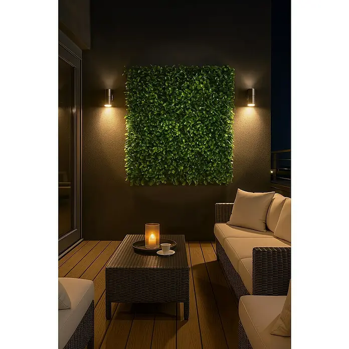 Jardín vertical Laurel - Plástico, L x An: 100 x 100 cm, 1 ud. - Espacio de estar al aire libre con sofá de ratán, mesa de centro con vela y pared verde, iluminado por apliques de pared.