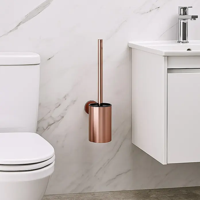 Camargue Carlit Escobillero mural - Altura: 34 cm, Oro rosa - Un escobillero de color oro rosa con soporte cuelga en una pared de mármol junto a un inodoro y un lavabo blancos.