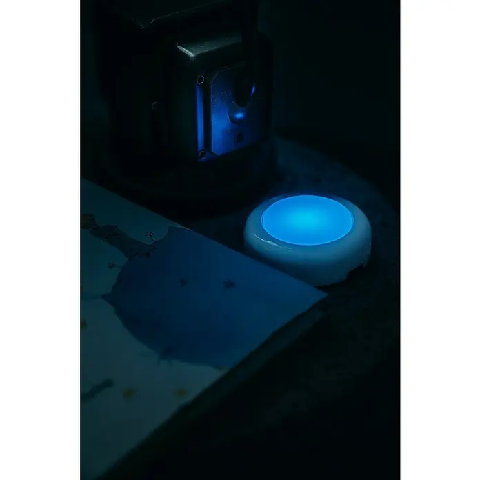 Osram Luz de armario LED Dot-It Twist & Shake - 1 luz, 0,5 W, Blanco - Luz nocturna azul brillante junto a un libro y una lámpara. La luz proporciona una iluminación suave y azul.