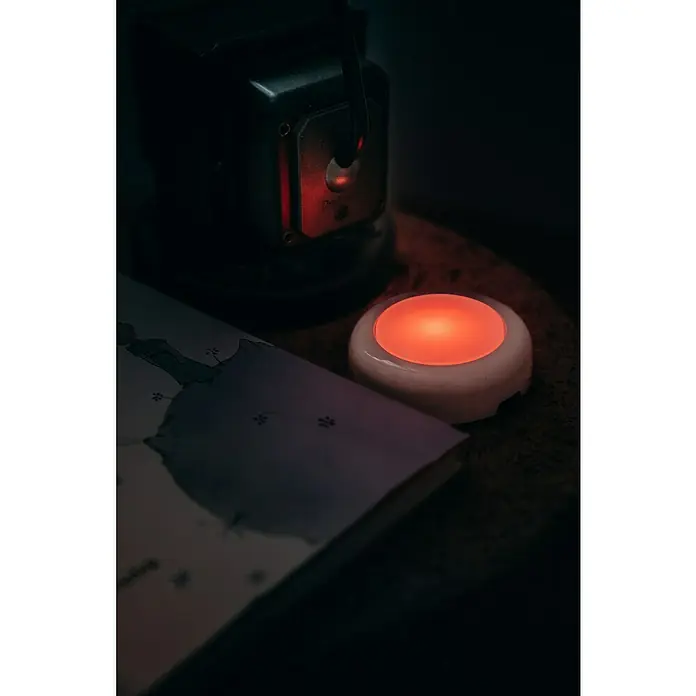 Osram Luz de armario LED Dot-It Twist & Shake - 1 luz, 0,5 W, Blanco - Una lámpara de mesa roja sobre una mesa junto a un libro, creando un ambiente cálido y acogedor.