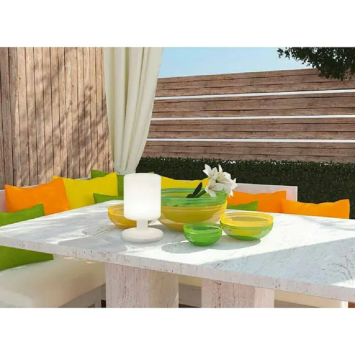 Trio Lighting Lámpara decorativa solar Barbados - 1,5 W, L x An x Al: 17 x 17 x 25,5 cm, Blanco, IP44 - Primer plano de una lámpara de mesa, un juego de cuencos de vidrio verde y amarillo sobre una mesa de exterior con cojines de colores.