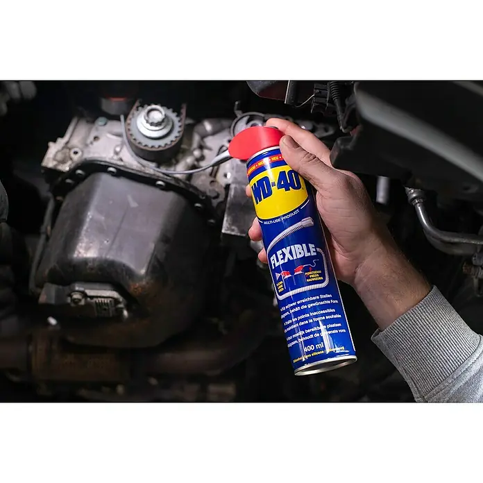 WD-40 Multiöl Flexible - 400 ml - Eine Hand hält eine Dose WD-40 Flexible Multi-Use Produkt vor einem Automotor, ideal für schwer zugängliche Stellen.