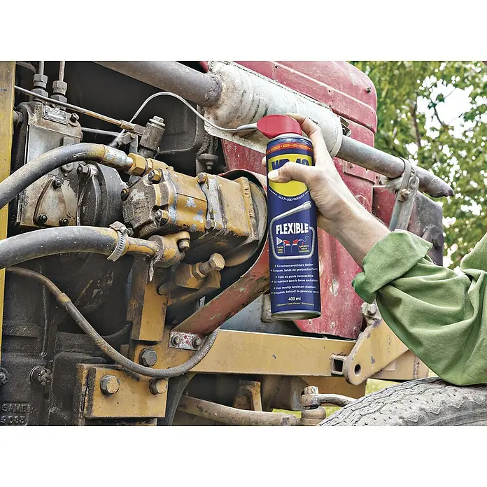 WD-40 Multiöl Flexible - 400 ml - Eine Hand hält eine Sprühdose WD-40 Flexible vor einem Traktormotor, um schwer zugängliche Stellen zu schmieren.