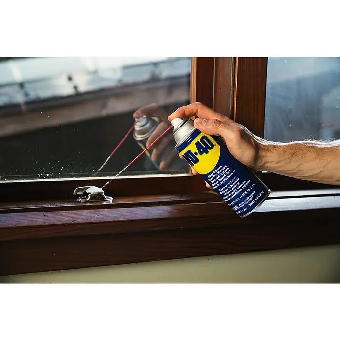 WD-40 Multiöl Classic - 100 ml - Eine Hand sprüht WD-40 auf einen Fensterriegel, um ihn zu lösen und vor Rost zu schützen. Das vielseitige Produkt ist ideal für Haus und Werkstatt.