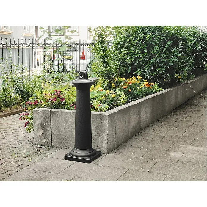 Proregal Asche-Mülleimer Rubbermaid Standaschenbecher mit Stahl-Inneneimer - Kunststoff, Schwarz - Die elegante, schwarze Säule mit quadratischer Basis und aufgesetztem Deckel steht vor einem Blumenbeet und akzentuiert den Außenbereich stilvoll.