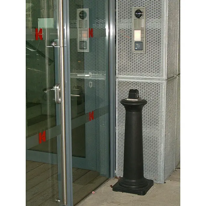 Proregal Asche-Mülleimer Rubbermaid Standaschenbecher mit Stahl-Inneneimer - Kunststoff, Schwarz - Schwarze Säule neben einem Eingang.