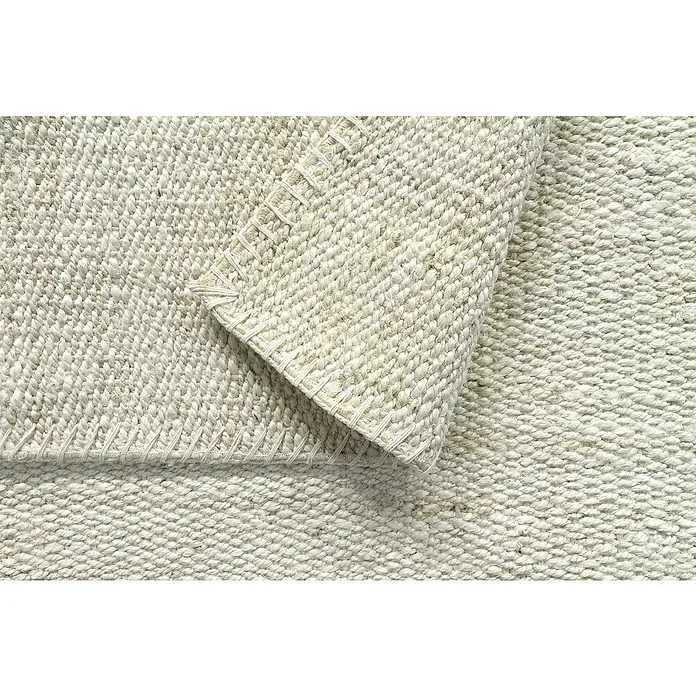 Alfombra de yute Córdoba - Blanco, 300 x 240 cm, 100% yute - Primer plano de una alfombra tejida con una esquina doblada que muestra su textura y borde cosido.