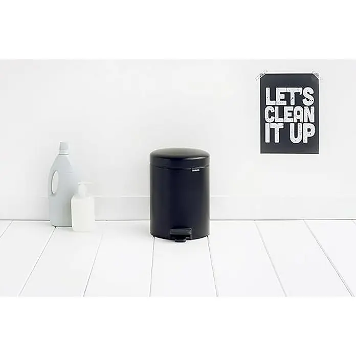 Proregal Treteimer Brabantia Klassischer Tretmülleimer mit Soft-Verschluss - 5 l, Metall, Metallik Schwarz - Dieses Bild zeigt einen schwarzen Treteimer, eine Reinigungsflasche und eine Seifenpumpe vor einer weißen Wand mit einem Poster.