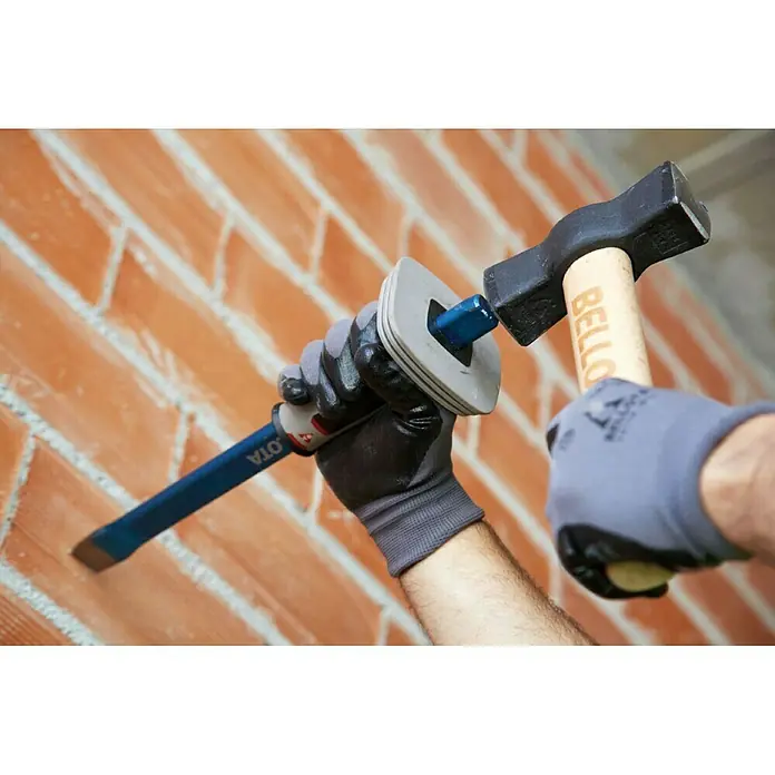 Bellota Maza 53080 - Largo: 43 mm, 1.400 g - Primer plano de manos con guantes protectores sosteniendo un cincel y un martillo para trabajar en una pared de ladrillo.