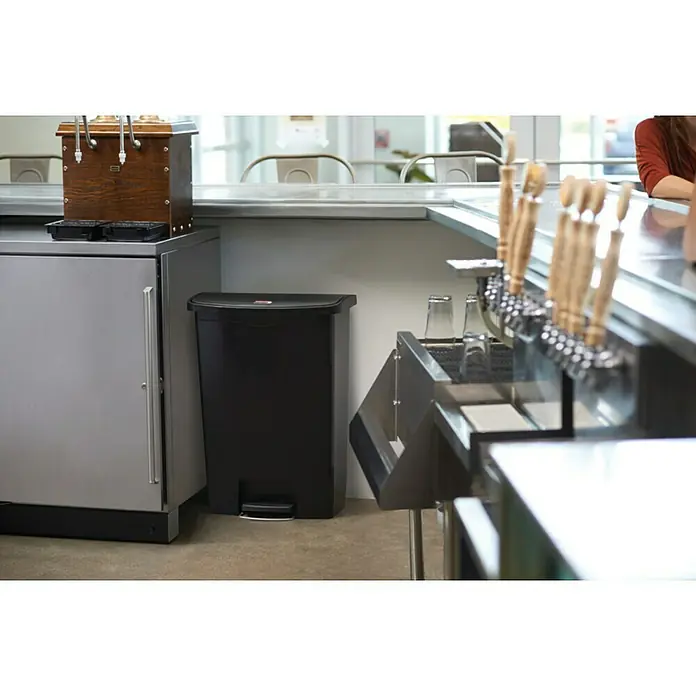 Proregal Treteimer Rubbermaid Slim Jim Step On Container Front Step Pedal-Abfalleimer - 68 l, Kunststoff, Schwarz - Hier ist ein schwarzer, rechteckiger Simplehuman-Treteimer mit einem roten Schiebeknopf am Deckel, der neben einem Edelstahlkühlschrank steht.