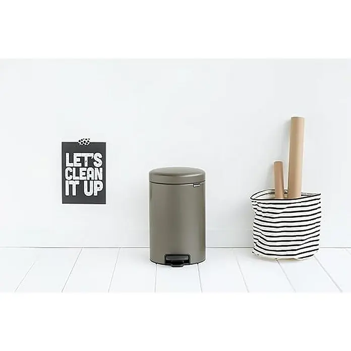 Proregal Treteimer Brabantia Klassischer Tretmülleimer mit Soft-Verschluss - 12 l, Metall, Platin - Ein grauer Tretabfalleimer steht neben einer gestreiften Stofftasche vor einer weißen Wand. Ein Poster mit der Aufschrift "Let's clean it up" hängt an der Wand.