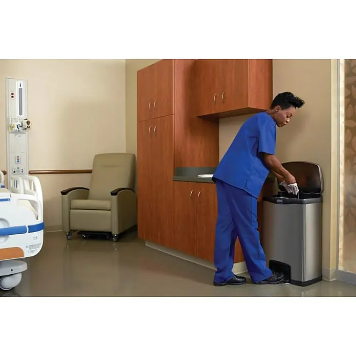 Proregal Treteimer Rechteckiger Treteimer aus gebürstetem Edelstahl - 45 l, Edelstahl, Silber - Eine medizinische Fachkraft in blauer Arbeitskleidung betätigt den Tretmechanismus eines modernen, silberfarbenen Abfalleimers in einem Krankenhauszimmer.