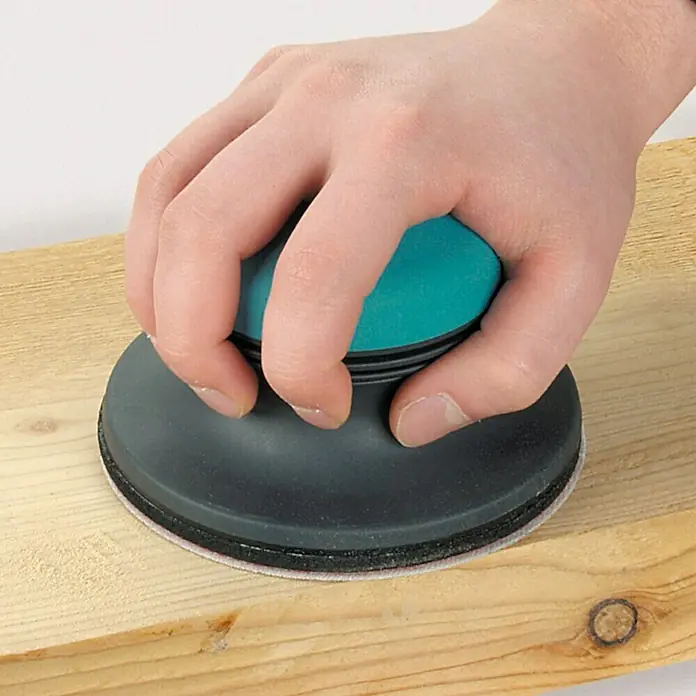 Juego de discos abrasivos - 125 mm, Grano: 40 - 60, 5 ud. - Primer plano de una lijadora manual en acción. La herramienta es sujetada por una mano mientras alisa una pieza de madera.