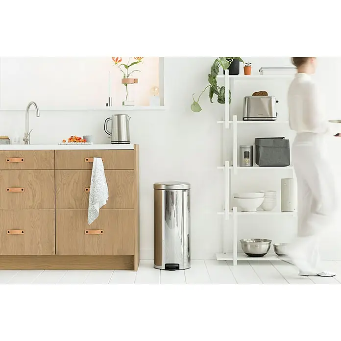 Proregal Treteimer Brabantia Klassischer Tretmülleimer mit Soft-Verschluss - 30 l, Metall, Edelstahl - Helles Kücheninterieur mit einem Edelstahl-Treteimer im Vordergrund, Küchenschränken aus Holz und einem weißen Regal mit Küchenutensilien.