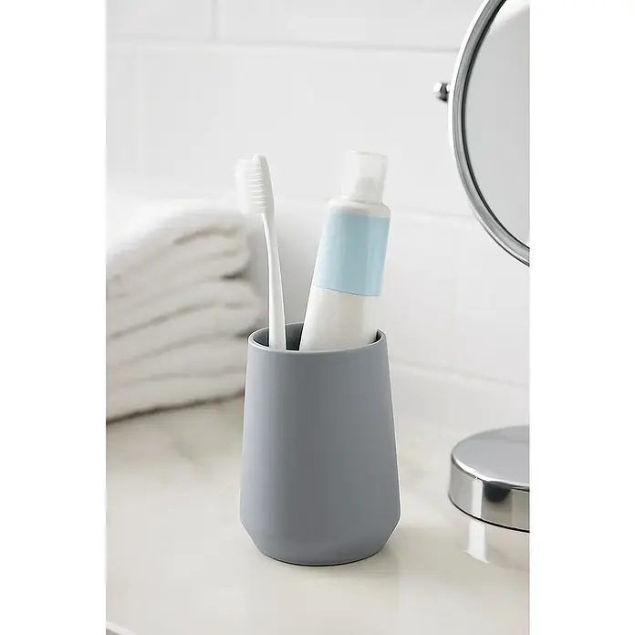Aquasanit Tower Portacepillos - Diámetro: 8 cm, Plástico, Blanco - Cepillo de dientes y pasta de dientes en un vaso gris sobre un tocador de baño.