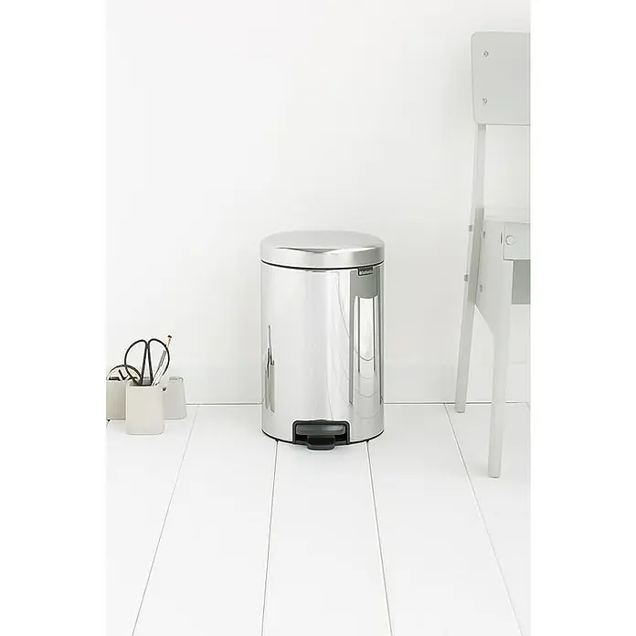 Proregal Treteimer Brabantia Klassischer Tretmülleimer mit Soft-Verschluss - 12 l, Metall, Edelstahl - Ein runder, silberfarbener Brantho-Möbel Mülleimer mit Fußpedal steht auf einem weißen Holzboden, neben einer Schreibtischgarnitur und einem Stuhl.