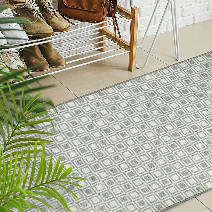 Teppichläufer Bray - Grau, 150 x 80 cm, 100 % Polyamid - Ein grauer Läufer mit geometrischem Muster liegt vor einem Schuhregal und einer Pflanze, die für einen stilvollen Eingangsbereich sorgt.