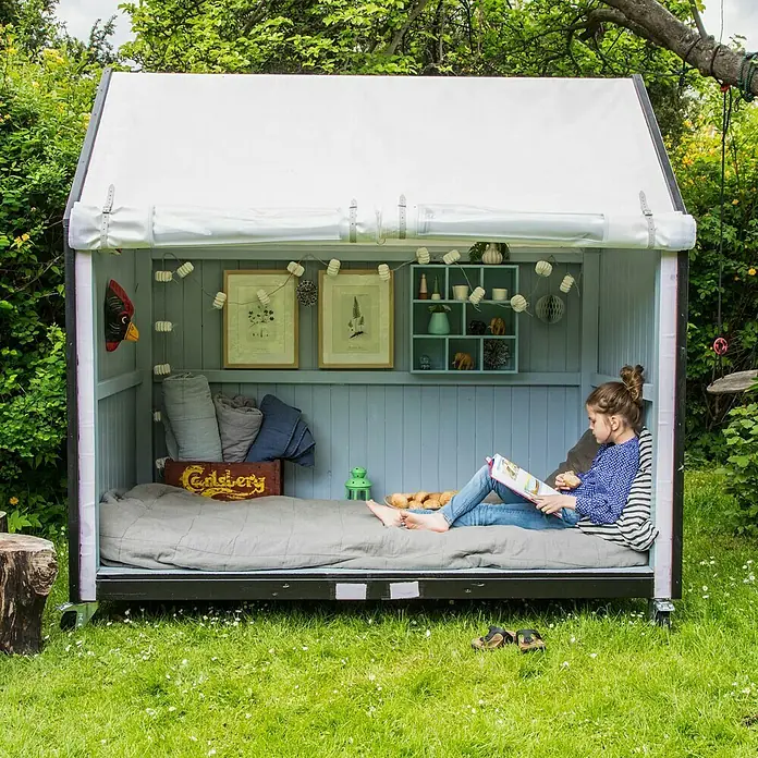 Plus Gewächshaus - Außenmaß inkl. Dachüberstand (B x T): 203 x 123 cm, 15 mm, Natur - Eine junge Frau entspannt in einem schicken, tragbaren Outdoor-Bett mit Rädern, ideal zum Lesen oder Entspannen im Garten.