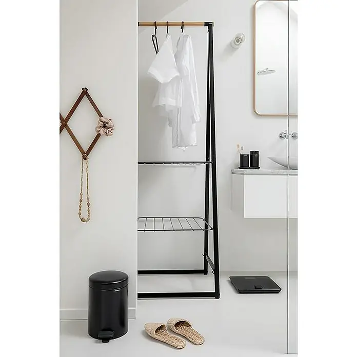 Proregal Treteimer Brabantia Klassischer Tretmülleimer mit Soft-Verschluss - 3 l, Metall, Metallik Schwarz - Ein modernes Badezimmer mit einem minimalistischen Kleiderständer aus schwarzem Metall, weißen Kleidungsstücken und Ablageflächen.