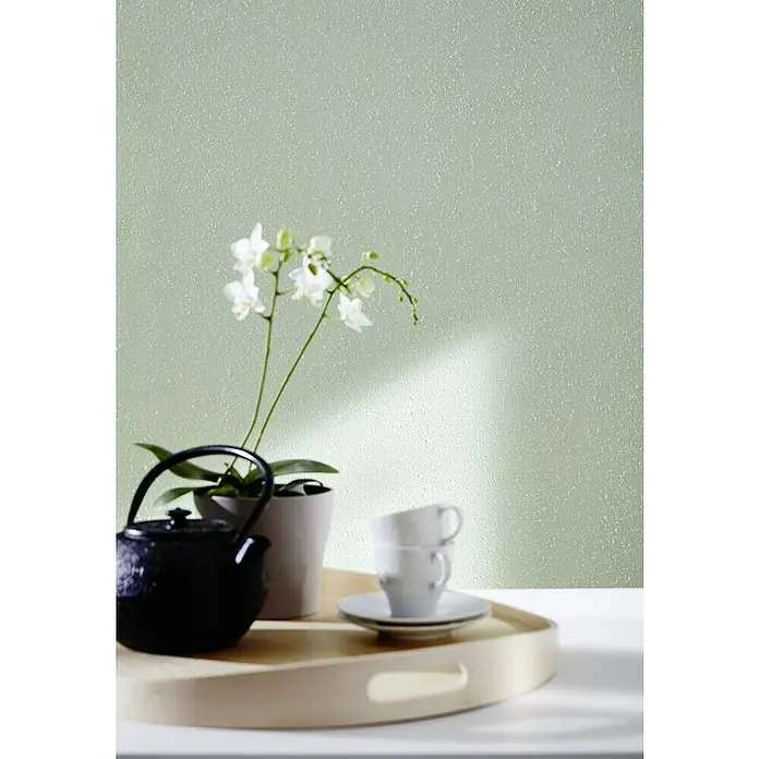 Knauf Putz-Abtönfarbe Compact Color - Jade, 2 g - Stillleben mit einer schwarzen Teekanne, Orchidee und zwei weißen Kaffeetassen auf einem hellen Holztisch vor einer hellgrünen Wand.