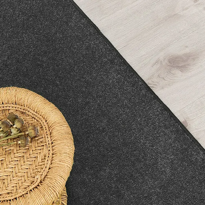 Kurzflorteppich Dynasty - Anthrazit, 100 x 100 cm, 100 % Polypropylen - Nahaufnahme eines schwarzen Teppichs auf einem hellen Holzboden, daneben ein runder Korb mit dekorativen Pflanzen.