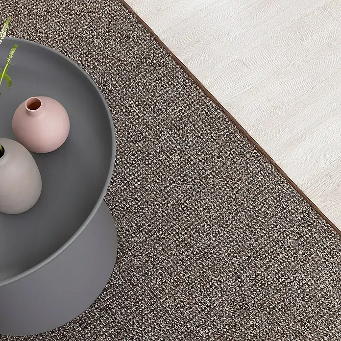Flachgewebeteppich Carlton - Braun, 200 x 200 cm, 100 % Polypropylen - Nahaufnahme eines braunen Sisalteppichs, der neben einem grauen Couchtisch mit zwei Vasen auf einem hellen Holzboden liegt.