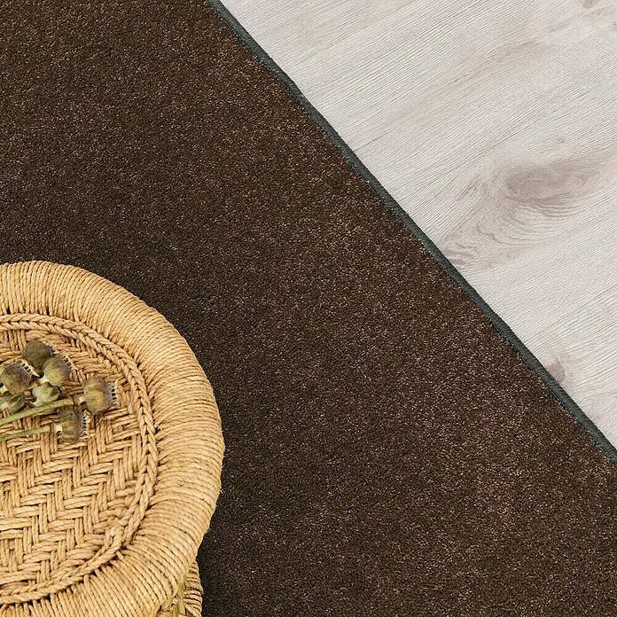Kurzflorteppich Dynasty - Schlamm, 100 x 100 cm, 100 % Polypropylen - Detailaufnahme eines braunen Teppichs mit gewebtem Beistelltisch und Holzboden, das die Textur und das Design des Teppichs hervorhebt.