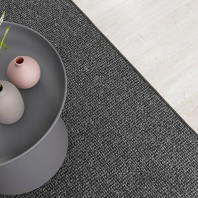 Flachgewebeteppich Carlton - Anthrazit, 200 x 200 cm, 100 % Polypropylen - Nahaufnahme eines grauen Teppichs mit Couchtisch und Vasen, der ein modernes und stilvolles Wohnambiente schafft.