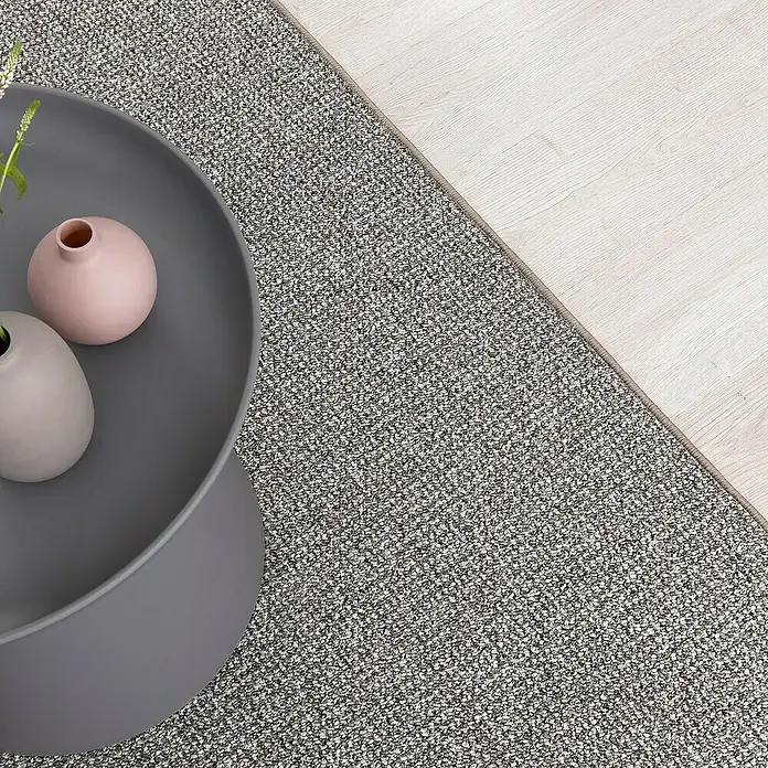 Flachgewebeteppich Carlton - Grau/Beige, 200 x 200 cm, 100 % Polypropylen - Nahaufnahme eines getufteten Velours-Teppichs in einem neutralen Grau, kombiniert mit einem modernen Couchtisch und hellen Holzboden.