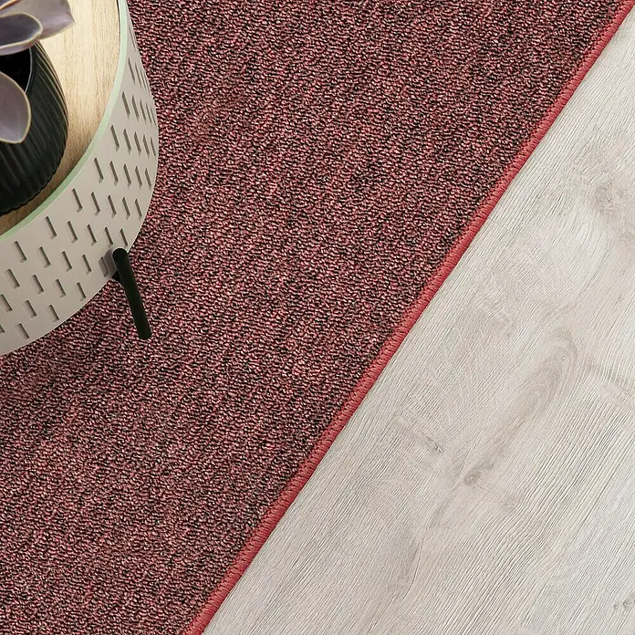 Flachgewebeteppich London - Weinrot, 200 x 200 cm, 100 % Polypropylen - Nahaufnahme eines roten Teppichs neben einem hellen Holzboden, der eine gemütliche und stilvolle Atmosphäre schafft.
