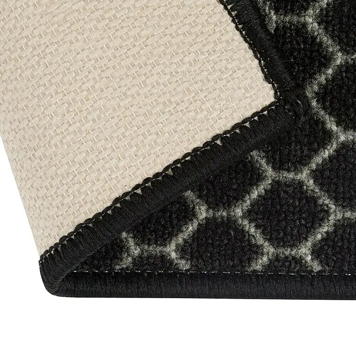 Teppichläufer Dundalk - Schwarz/Weiß, 150 x 80 cm, 100 % Polyamid - Nahaufnahme einer schwarzen Teppichkante mit geometrischem Muster und beiger Rückseite, die die Textur und Verarbeitung des Produkts hervorhebt.