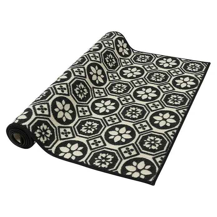 Teppichläufer Asaph - Schwarz/Weiß, 200 x 80 cm, 100 % Polyamid - Eine aufgerollte Fußmatte mit einem schwarz-weißen Blumenmuster auf einem schwarzen Hintergrund, die ein elegantes Design für den Innenbereich bietet.