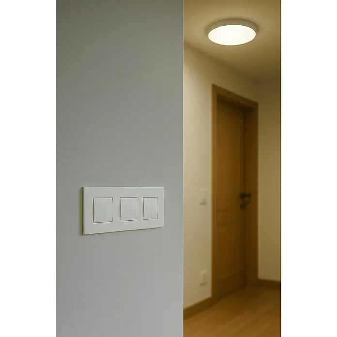 Bticino Living Light Marco - Blanco, Modelo de mecanismos: x 3, Plástico, Colocar - Un primer plano de una placa de interruptor de luz triple blanca en una pared, con la luz encendida al fondo iluminando la habitación.