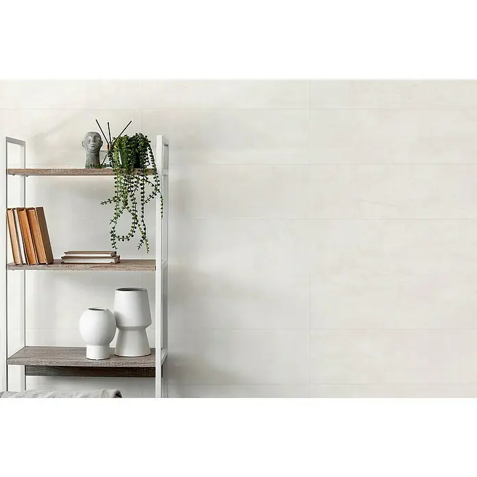 Revestimiento de pared Lyra - 29,5 x 90 cm, Marfil, Mate - Estantería moderna con elementos decorativos como libros, jarrones y una planta frente a una pared clara estructurada horizontalmente.
