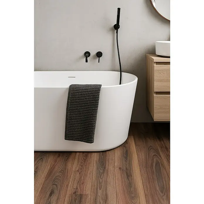 LOGOCLIC Aquaprotect Laminado Roble Renaissance - 1.288 x 195 x 12 mm, Roble Renaissance, AC5, Resistente al agua - Un baño moderno con bañera blanca, accesorios negros, toalla de gofre gris y piso de madera, creando un espacio de baño sereno y elegante.